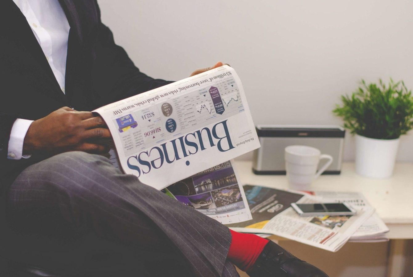 Printed newspaper business pages spread across a wooden desk